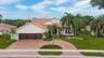 Stucco exterior with a tile roof, three-car garage, brick paver driveway, and mature landscaping