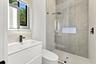 Floating vanity with integrated sink, backlit mirror, matte black fixtures, walk-in shower with glass enclosure, and wall-mounted rain shower head
