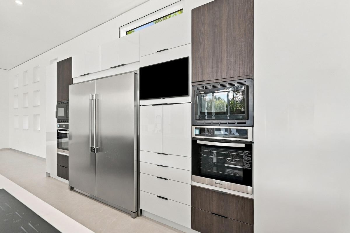 Contemporary kitchen featuring stainless steel dual-door refrigerator, integrated wall-mounted oven and microwave, flat-panel cabinetry in white and w