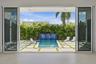 Seamless indoor-outdoor living with floor-to-ceiling glass doors opening to a resort-style backyard featuring a geometric paved terrace, resort pool w