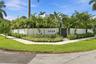 Modern architectural entry featuring a striking white perimeter wall with integrated address signage, lush tropical landscaping including mature palms