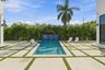 Rectangular swimming pool with a tile waterfall feature, surrounded by paver patio with artificial grass accents, and a lush privacy hedge