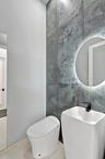 Modern bathroom featuring a sleek vessel sink with matte black wall-mounted faucet, illuminated circular mirror with integrated lighting, and a contem