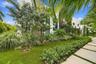 Lush landscaped grounds featuring mature palms and tropical plantings, manicured lawn, and linear concrete pathway leading to the residence