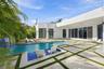 Modern residence featuring a resort-style swimming pool with crystal-clear waters, expansive hardscape patio with geometric inset planting beds, matur
