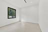 Bright, minimalist bedroom showcasing polished concrete flooring, clean white walls, and abundant natural light from a black-framed window