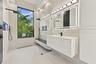 Spa-inspired primary bathroom featuring a frameless glass-enclosed shower with rainfall showerhead and handheld fixture, floating vanity with integrat