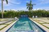 Resort-style lap pool with lane markers and deep blue tile accents, flanked by manicured lawn strips and mature palm landscaping