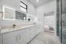 Spacious Jack-and-Jill bathroom featuring a glass-enclosed shower with blue-toned tile, a dual vanity with light-colored countertops, white cabinetry 
