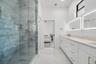 Jack-and-Jill bathroom featuring dual vanity with quartz countertops and integrated sinks, illuminated mirrors, frameless glass shower enclosure, and 