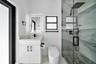 Frameless glass shower enclosure with a rainfall showerhead, white vanity with a light-colored countertop, and an illuminated mirror