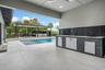 Expansive outdoor living area featuring a swimming pool, covered patio, outdoor kitchen, and large format tile flooring
