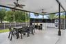 Expansive covered patio with an outdoor kitchen, featuring a central island with a sink, white cabinetry, and a dark tiled backsplash