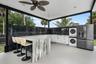 Covered outdoor kitchen featuring a large stone-finish island, white cabinetry, dark tile backsplash, a stacked washer and dryer, and a stainless stee