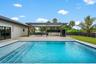 Rectangular swimming pool with integrated steps, adjacent to a covered patio featuring an outdoor kitchen