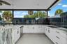 Outdoor kitchen featuring white cabinetry, a built-in cooktop, integrated dishwasher, and a bar seating area