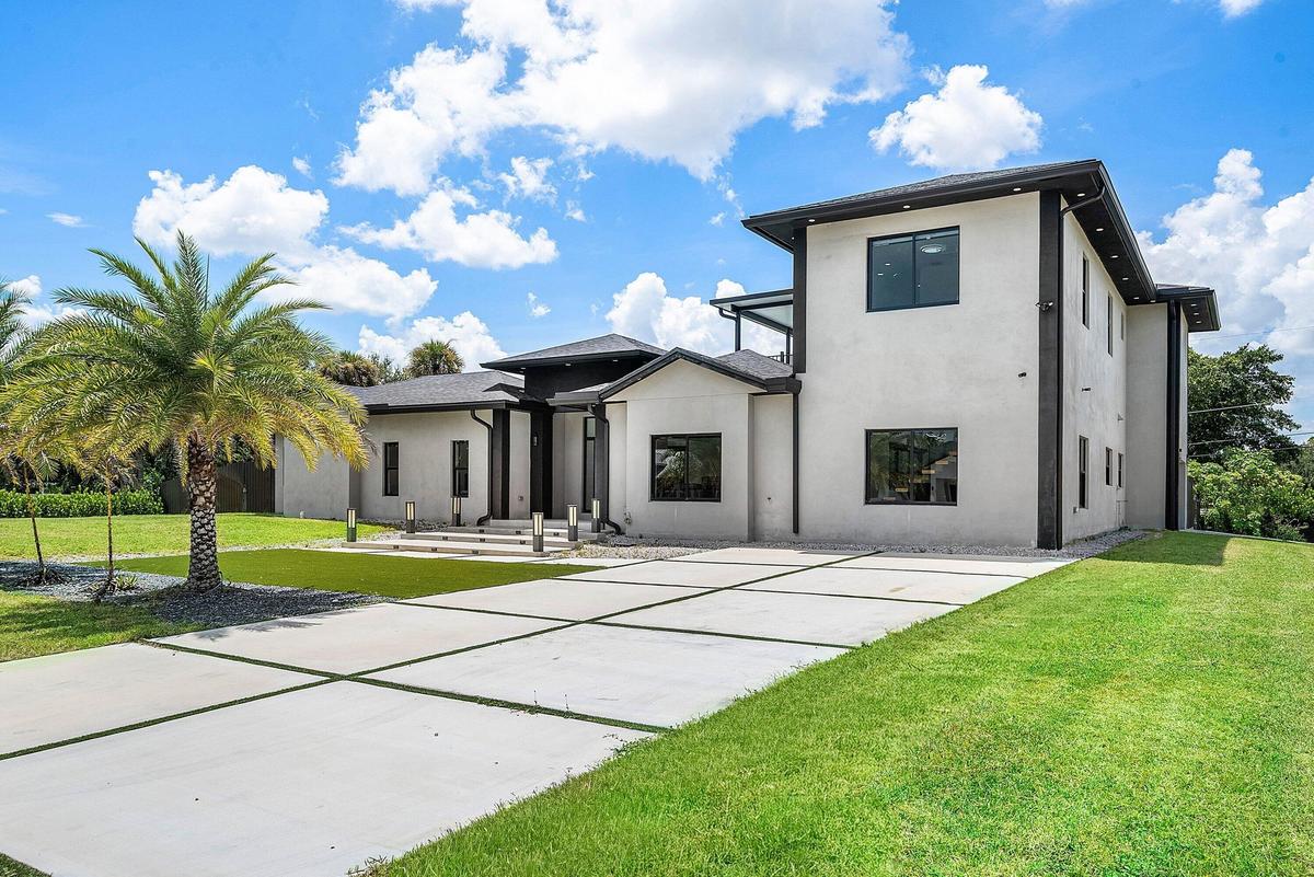 Contemporary architectural design with a multi-level structure, a concrete driveway featuring grass inlays, a large front lawn, and a prominent palm t