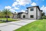 Contemporary architectural design with a multi-level structure, a concrete driveway featuring grass inlays, a large front lawn, and a prominent palm t
