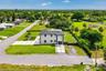 Two-story stucco exterior, dark roof, expansive green lawn, modern concrete driveway, and black fencing