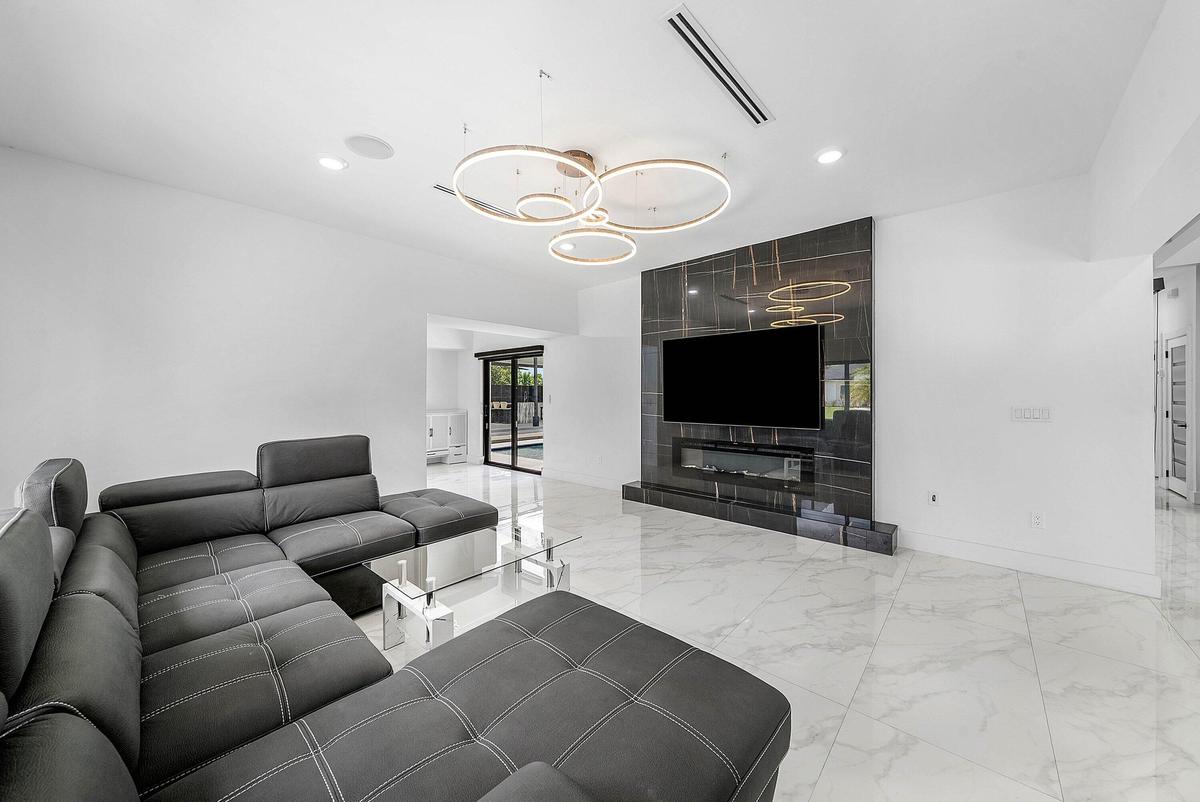 Open-concept living space with large format tile flooring, a dark accent wall with an integrated electric fireplace, and a contemporary ceiling fixtur