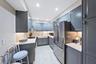 Galley kitchen featuring gray cabinetry, stainless steel appliances, a white farmhouse sink, and under-cabinet lighting