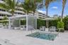 Built-in spa with steps and grab rails, surrounding stone-finish paving, pergola structure, and extensive landscaping