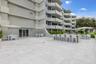 Expansive outdoor patio with stone-finish pavers, multiple seating areas, a built-in bar, and a multi-story building exterior with individual balconie