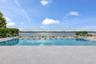 Expansive outdoor pool with integrated steps, surrounded by a light-toned paved deck, and featuring a clear glass safety barrier