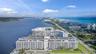 Waterfront residential building with multiple balconies, positioned along a waterway with a prominent ocean backdrop