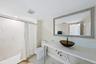 White tile flooring, full wall mirror, glass vessel sink, white countertop, and tiled shower surround