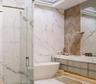 Freestanding soaking tub, glass-enclosed shower, wall-mounted vanity with integrated lighting, wood-finish chevron accent wall, and skylight