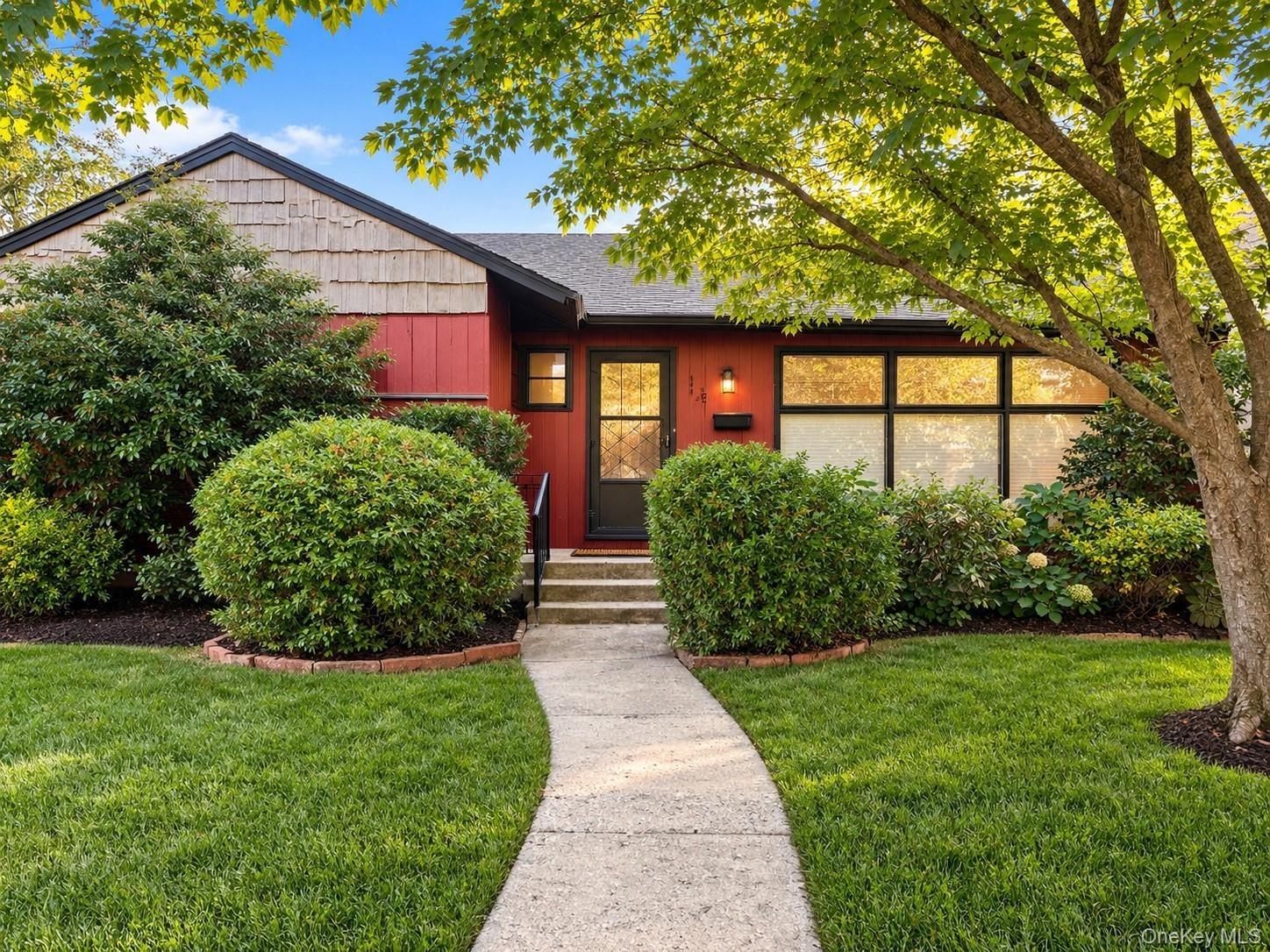 Red exterior with wood shake siding, a concrete walkway, mature tree, and established landscaping