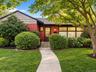 Red exterior with wood shake siding, a concrete walkway, mature tree, and established landscaping