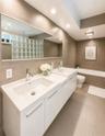 Dual vanity with integrated sinks and chrome fixtures, large rectangular mirror, recessed lighting, and a glass block shower wall