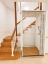 Built-in home elevator with patterned wood-finish flooring, staircase with wood treads, and white wall paneling