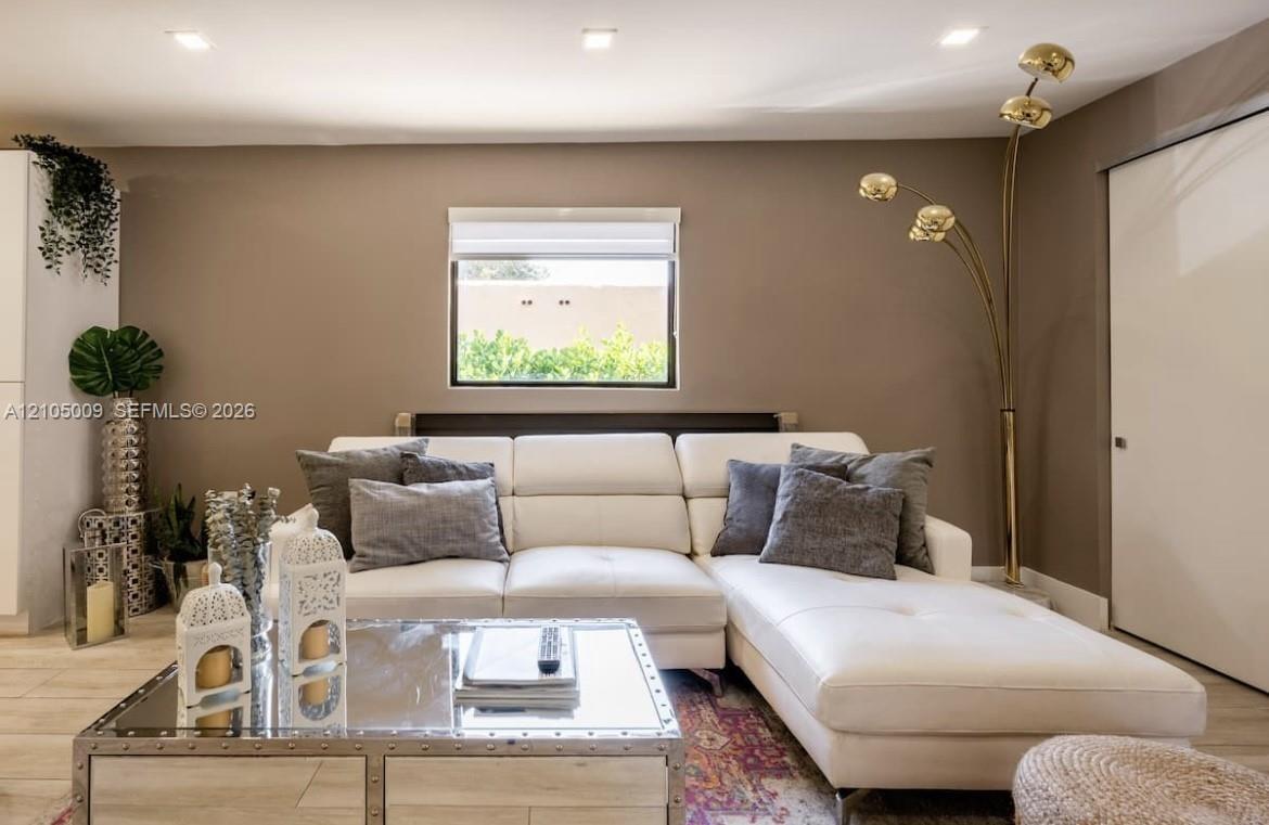 Recessed ceiling lighting, a single window with blinds, and light-toned walls create an inviting living space