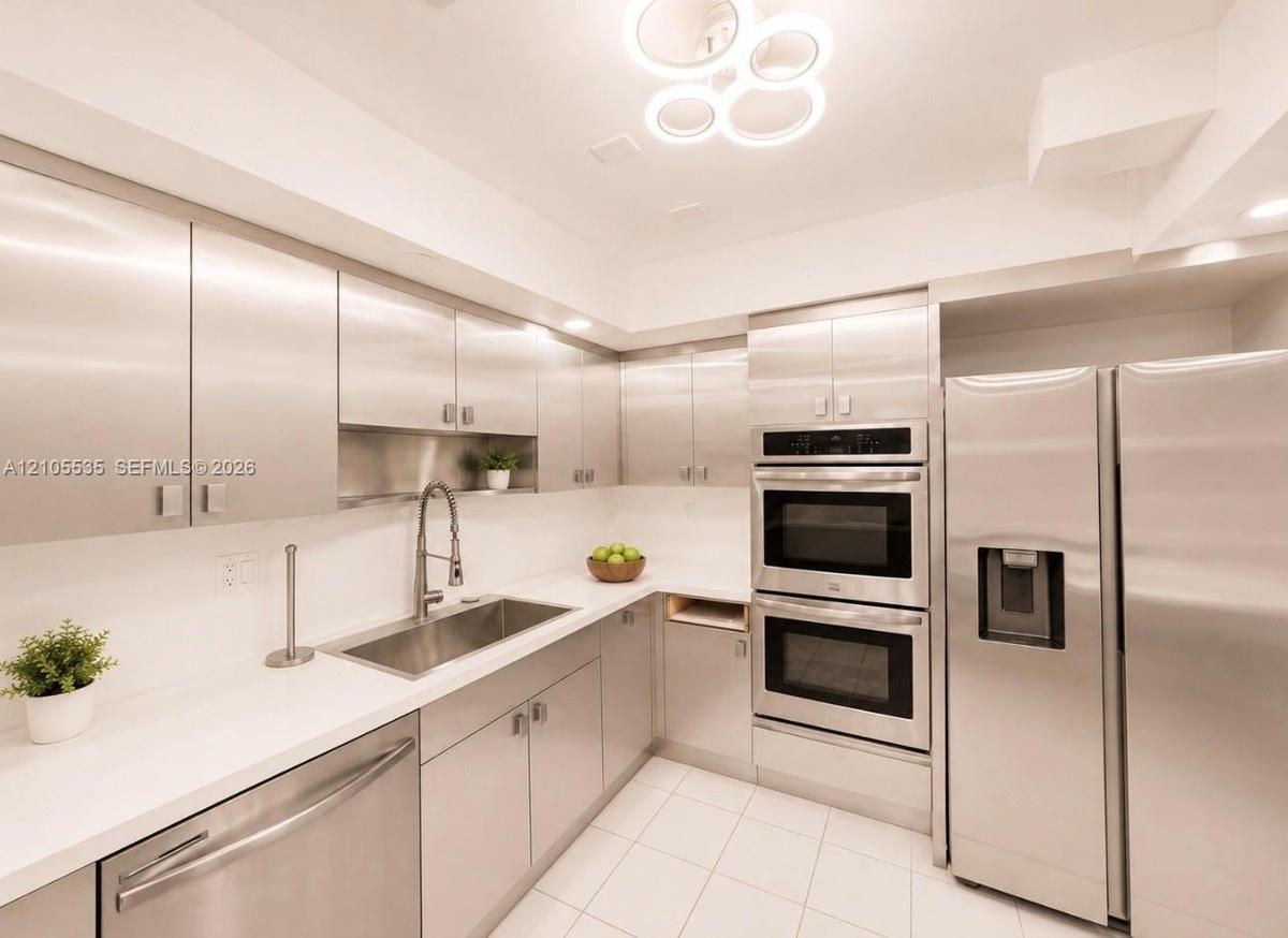 Stainless steel appliances, white tile flooring, white countertops, built-in double ovens, and a contemporary ceiling fixture