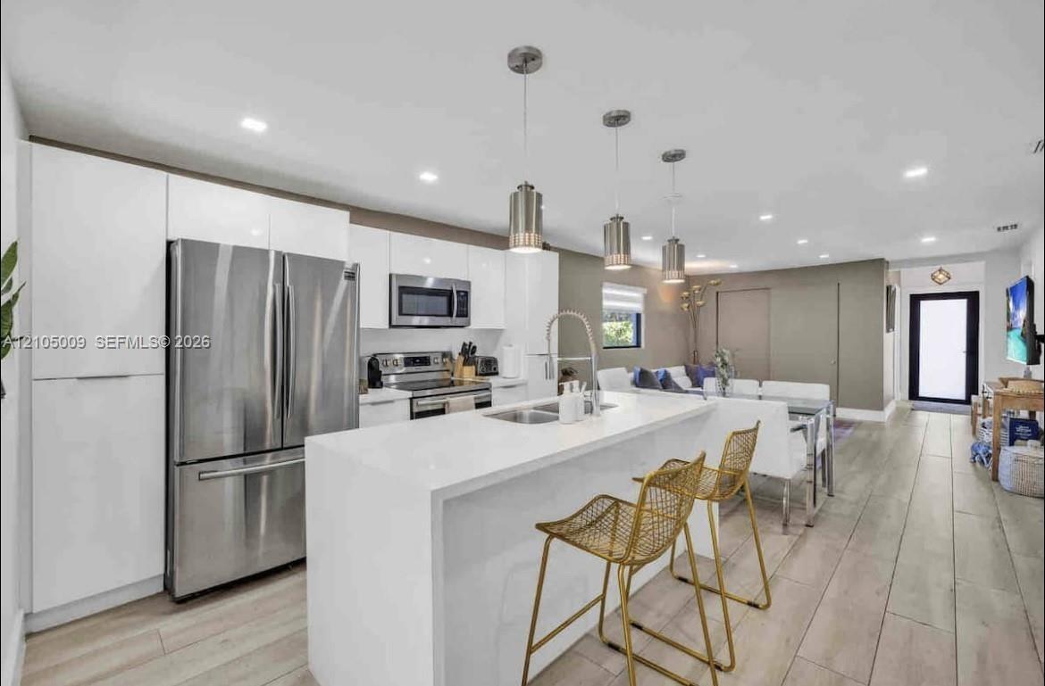 Modern kitchen featuring white cabinetry, stainless steel appliances, a center island with sink, and pendant lighting