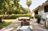 Expansive backyard featuring a wood-slat patio, a manicured lawn, lush perimeter hedging, and a white stucco exterior with dark-framed sliding glass d