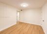 Wood-finish flooring, white paneled wall, flat panel interior door, ceiling-mounted light fixture, white baseboards