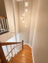 Staircase featuring wood steps, wood handrail, white balusters, and a multi-pendant light fixture