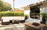 Exterior wood deck with a built-in fire pit, privacy hedging, concrete steps, and dark-framed sliding glass doors