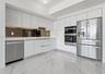Sleek kitchen featuring white flat-panel cabinetry, stainless steel appliances, a mirrored backsplash, and large format tile flooring