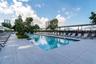 Resort-style pool with integrated steps, surrounded by large format tile decking, shaded lounge areas, and mature landscaping