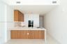 Kitchen featuring contemporary wood-finish and white cabinetry, built-in stainless steel appliances, a large island with an undermount sink, and light