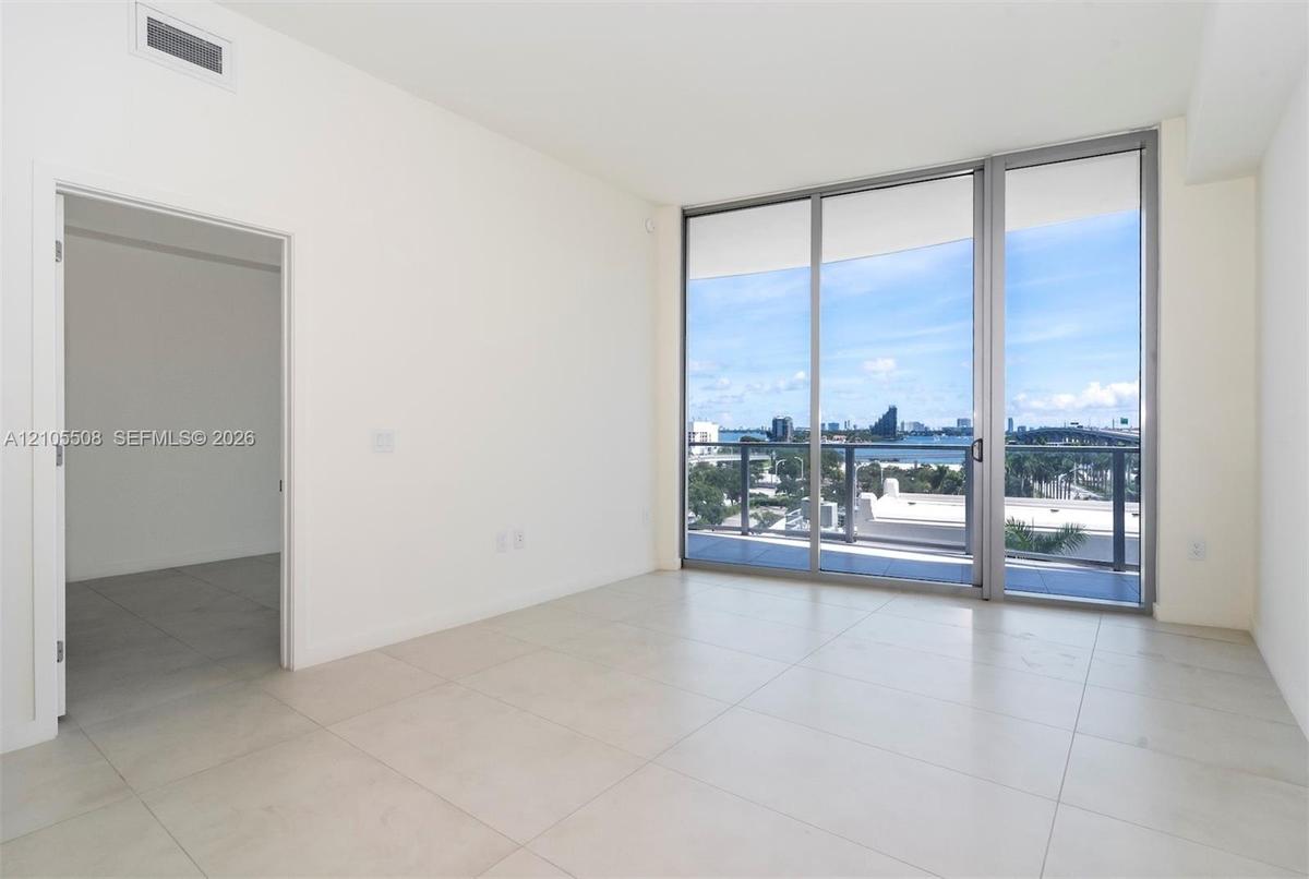Sliding glass doors opening to a balcony with metal railings, tile flooring, and white walls