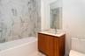 Bathtub with subway tile surround, wood-finish vanity with countertop, and rectangular wall-mounted mirror