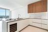 Modern kitchen featuring light wood-finish cabinetry, white flat-panel lower cabinetry, integrated stainless steel sink, under-cabinet lighting, and a
