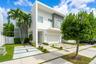 Modern architectural design with a white and gray exterior, integrated garage, concrete and grass paver driveway, and established landscaping