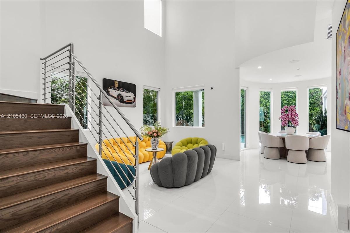 Two-story entry with wood-finish staircase, stainless steel railing, high ceilings, large format tile flooring, and multiple windows